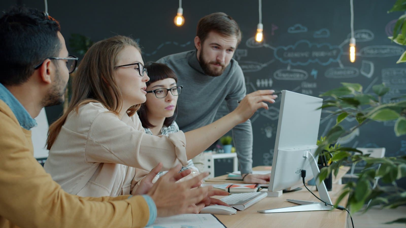 Four colleagues gathered around a desktop screen in an agency studio, one pointing at the display