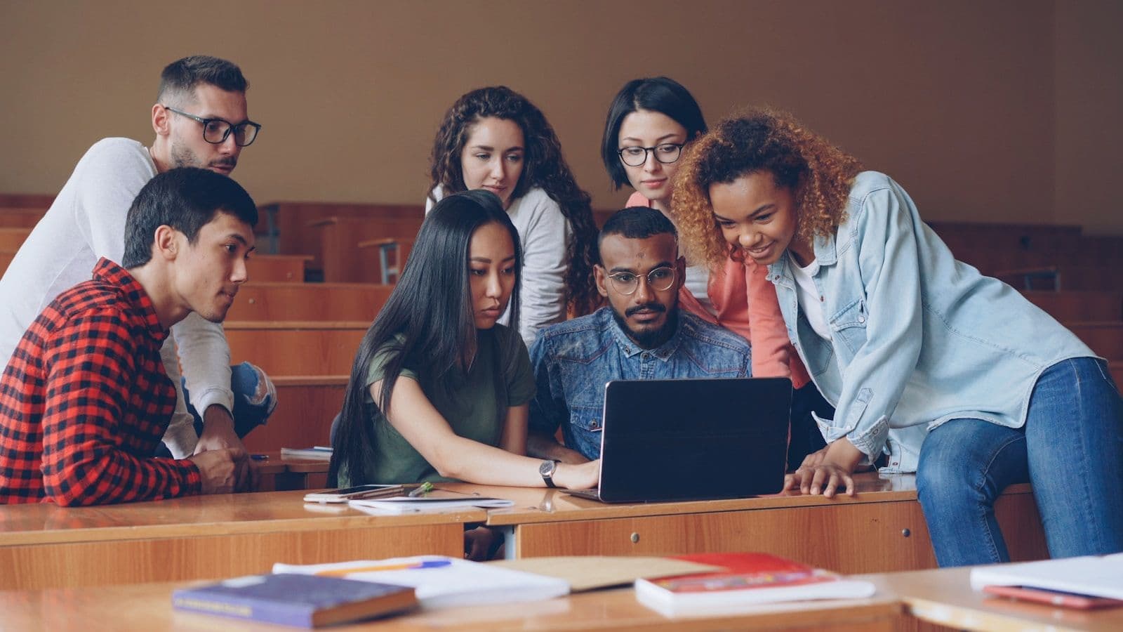 University students gathered around one laptop in a lecture hall